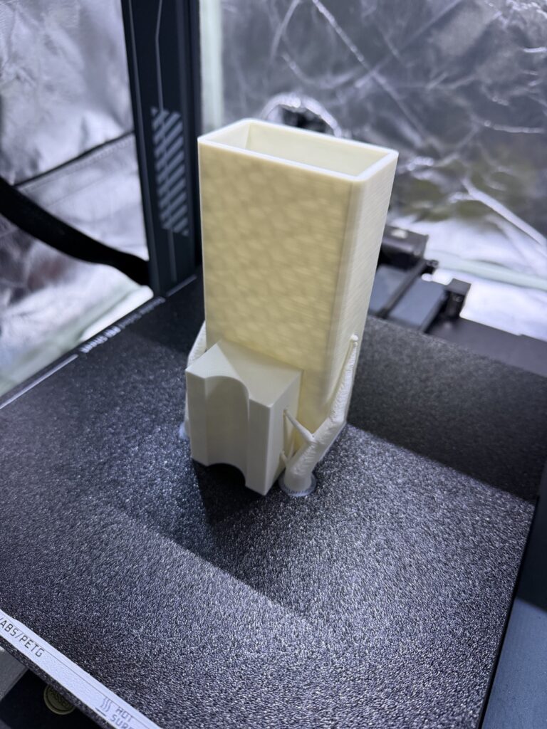 Fresh white PETG print on the printer bed: a hollow rectangular body with an integrated curved saddle for clamping to a pole.