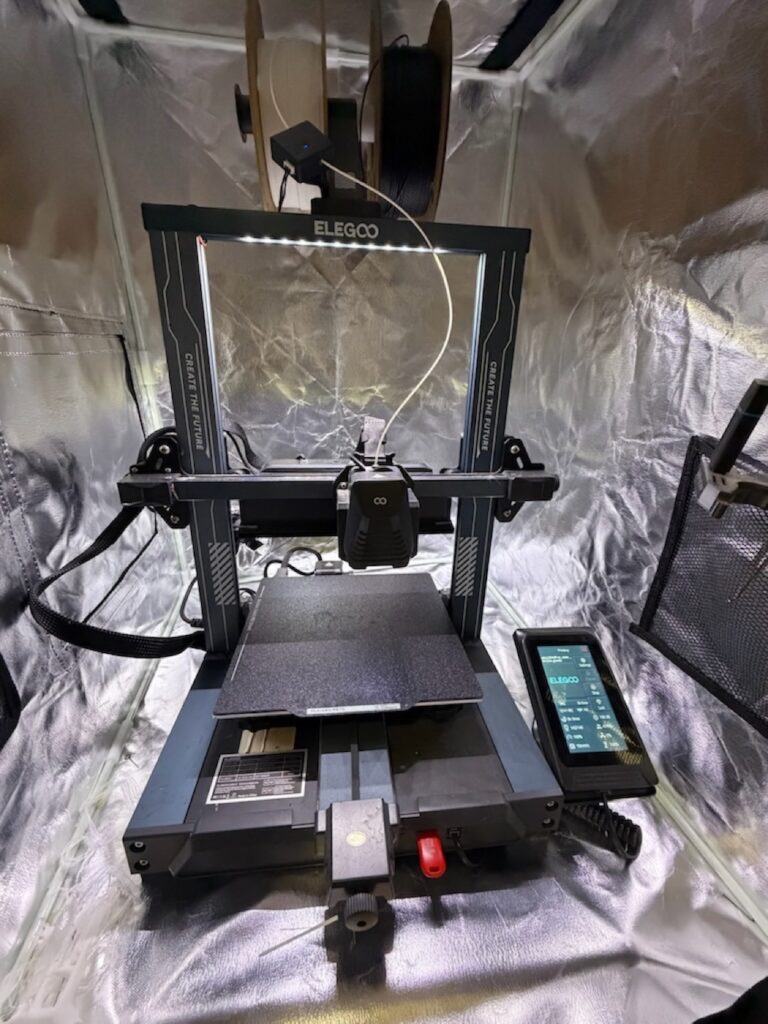 Elegoo desktop 3D printer inside a silver tent enclosure, empty print bed, with white filament loaded for the PETG case.
