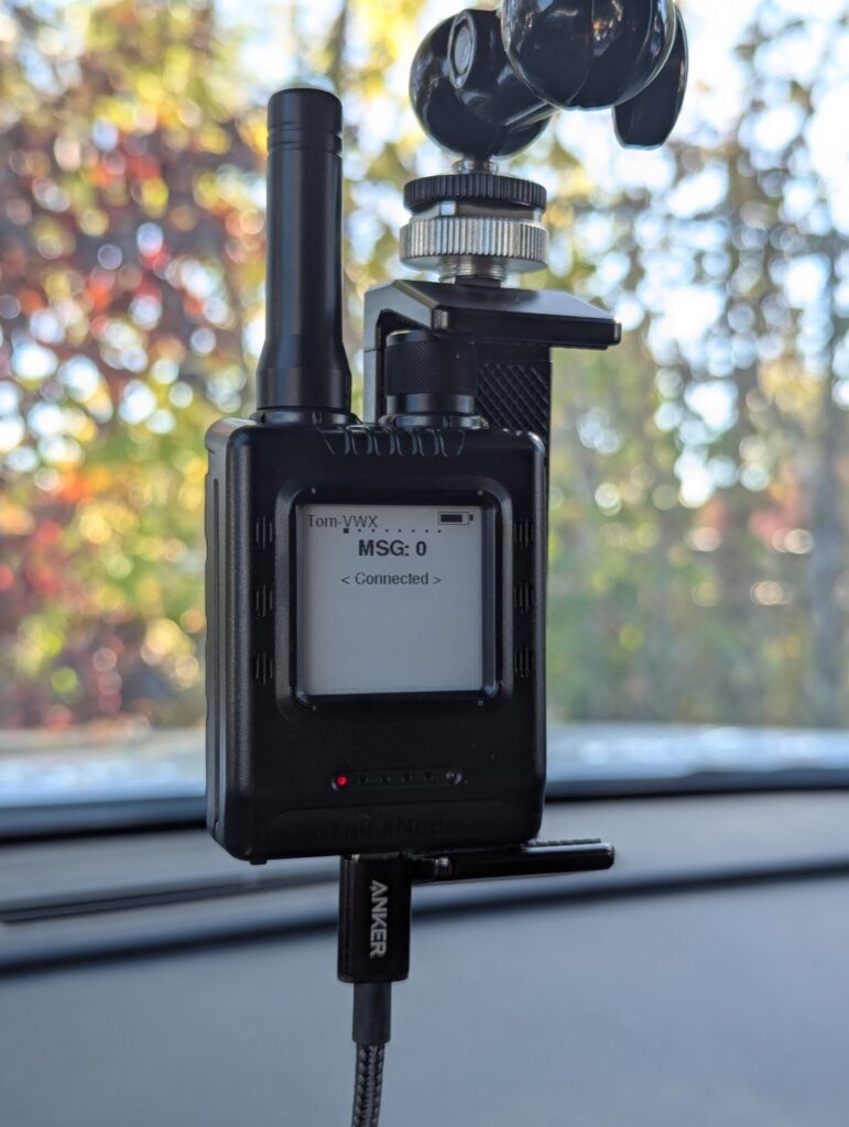 Black Elecrow ThinkNode M1 handheld on a car dash mount. The e-ink screen shows Tom-VWX, MSG 0, and Connected, with a USB-C cable plugged in at the bottom.